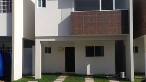 A modern two-story residential building with a flat roof, a front porch, and a small front yard with a pathway.