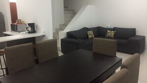 A modern living room with a dark sofa, two patterned cushions, a coffee machine, and a white countertop.