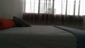 A bed with a white mattress, an orange pillow, and a grey pillow.