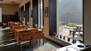 A modern interior with wooden tables and chairs, large windows with a view of a mountainous landscape, and a bookshelf. - Korea Palace Hotel (Pyeongchang)