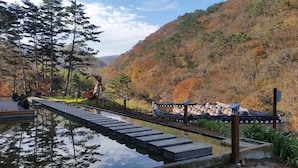 A traditional Japanese garden with a stone bridge over a reflective water body, surrounded by autumn-colored trees and a mountainous backdrop. - Korea Palace Hotel (Pyeongchang)