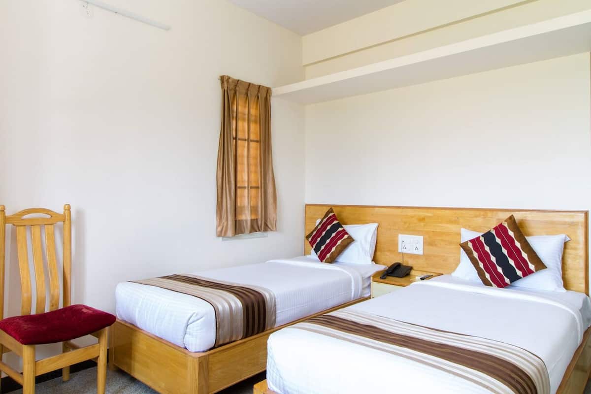 A hotel room with two single beds, a wooden chair, a nightstand, and a telephone.