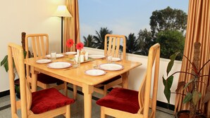 A dining table set for four with red cushions, a lamp, and a view of palm trees. - Hoppers Stop Yelahanka (Bengaluru)