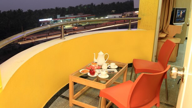 A balcony with a table set for tea, two chairs, and a view of a highway at dusk. - Hoppers Stop Yelahanka (Bengaluru)