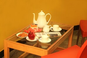 A breakfast setup on a glass table with a teapot, cups, a plate with cookies, an apple, and a newspaper. - Hoppers Stop Yelahanka (Bengaluru)