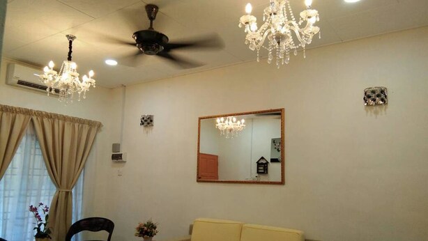 Una sala de estar con un sofá amarillo, dos sillones, una araña, un ventilador de techo y un espejo grande en la pared.