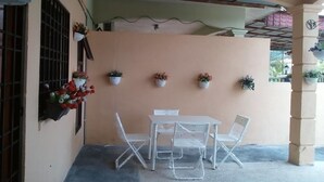 Un pequeño patio con una mesa, sillas, plantas en macetas y una ventana con reja de metal.