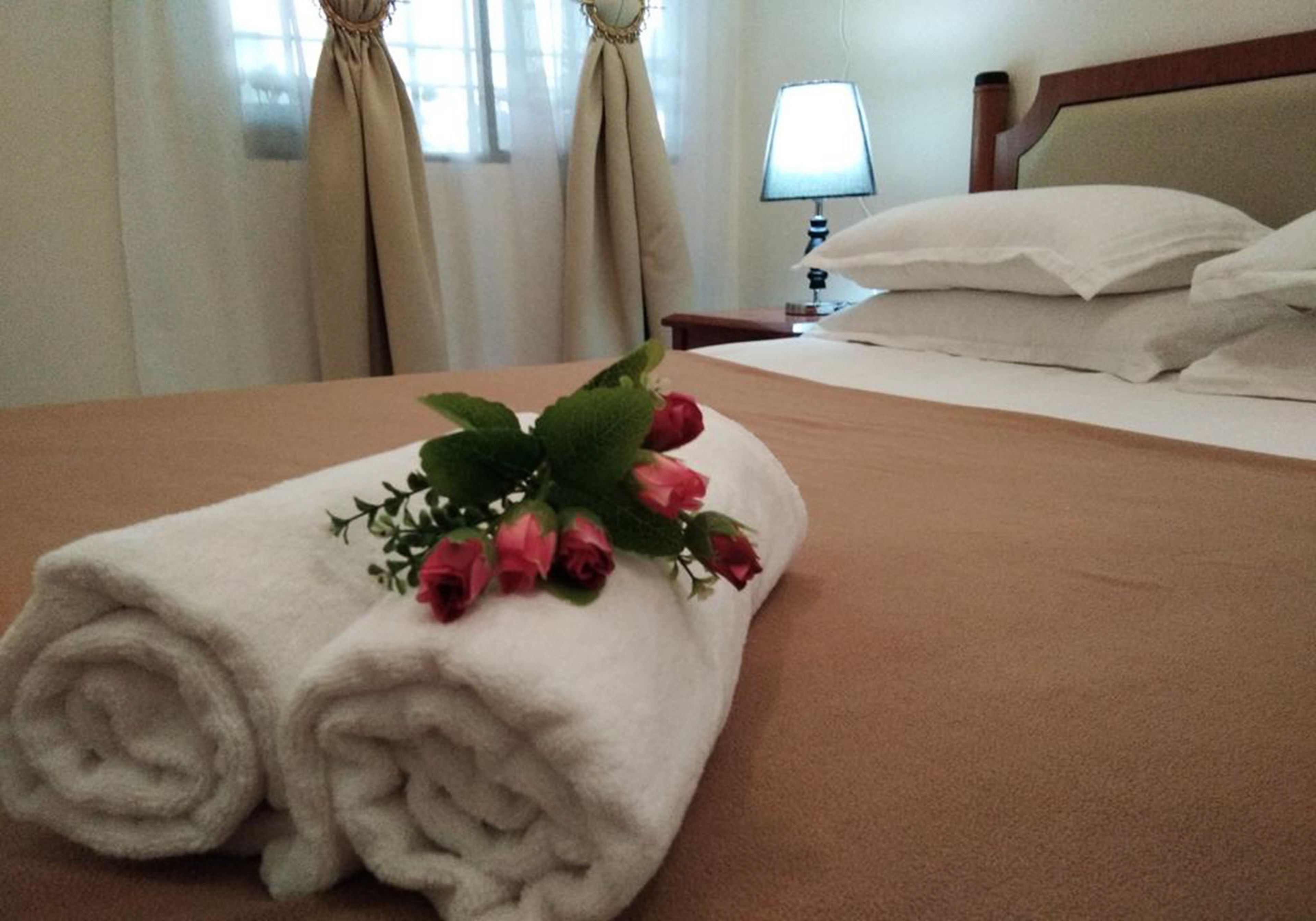 A neatly made bed with a rolled white towel and a bouquet of pink roses.