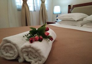 A neatly made bed with a rolled white towel and a bouquet of pink roses.