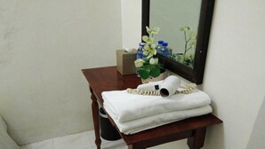 Una pequeña mesa de madera con una toalla blanca doblada, un secador de pelo y un florero con flores blancas.