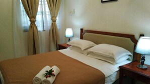 Una habitación de hotel con cama, mesita de noche, lámpara y cortinas.