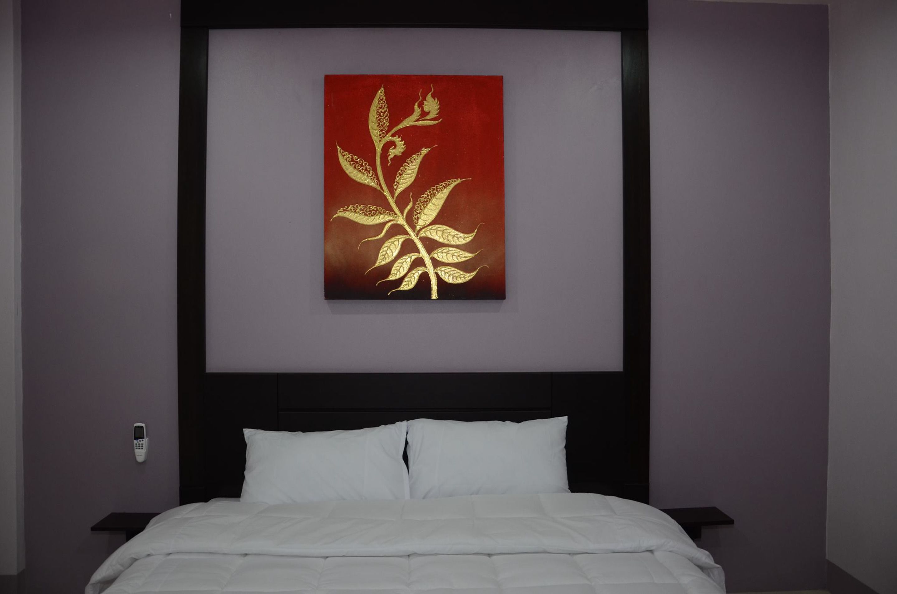 Habitación de hotel con una cama, una mesita de noche, un teléfono en la pared y una obra de arte roja y dorada sobre la cama.