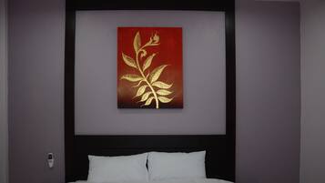 Habitación de hotel con una cama, una mesita de noche, un teléfono en la pared y una obra de arte roja y dorada sobre la cama.