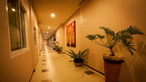 A hotel corridor with a tiled floor, potted plants, and a large painting on the wall. - Chiang Kham Grand Villa (Chiang Kham)