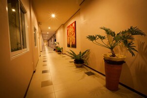 Un pasillo de hotel con suelo de baldosas, plantas en macetas y un cuadro grande en la pared.