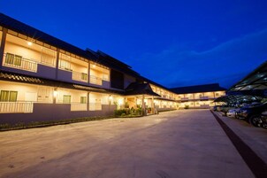 Un hotel con varios pisos, una zona de estacionamiento techada y un exterior bien iluminado al anochecer.