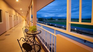 A corridor with a balcony, a table with chairs, and a view of a landscape with buildings and a train track. - Chiang Kham Grand Villa (Chiang Kham)