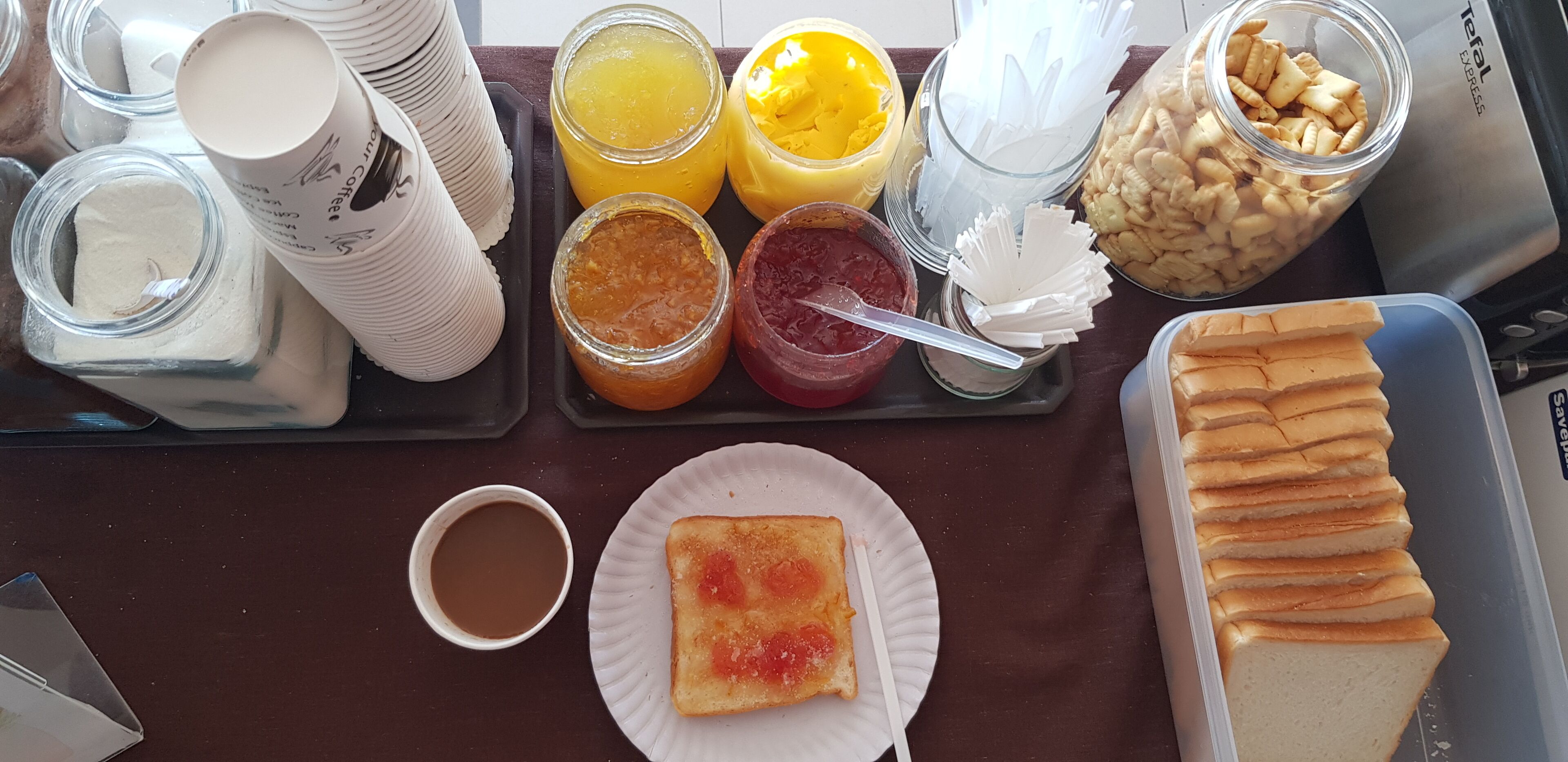 Una bandeja de desayuno con diversos alimentos y condimentos, como tostadas, jugo y pasteles.