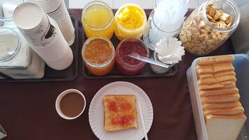 Una bandeja de desayuno con diversos alimentos y condimentos, como tostadas, jugo y pasteles.
