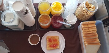 Una bandeja de desayuno con diversos alimentos y condimentos, como tostadas, jugo y pasteles.