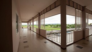 A corridor with large windows and a view of a road and greenery. - Chiang Kham Grand Villa (Chiang Kham)