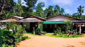 Ein bungalowähnliches Gebäude mit Ziegeldach, umgeben von üppiger Vegetation und Palmen.