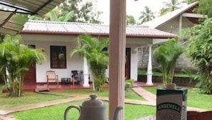 Ein Tisch gedeckt mit einem Teekessel, einer Kaffeetasse und einer Milchflasche, mit Blick auf ein Haus und einen Garten im Hintergrund.
