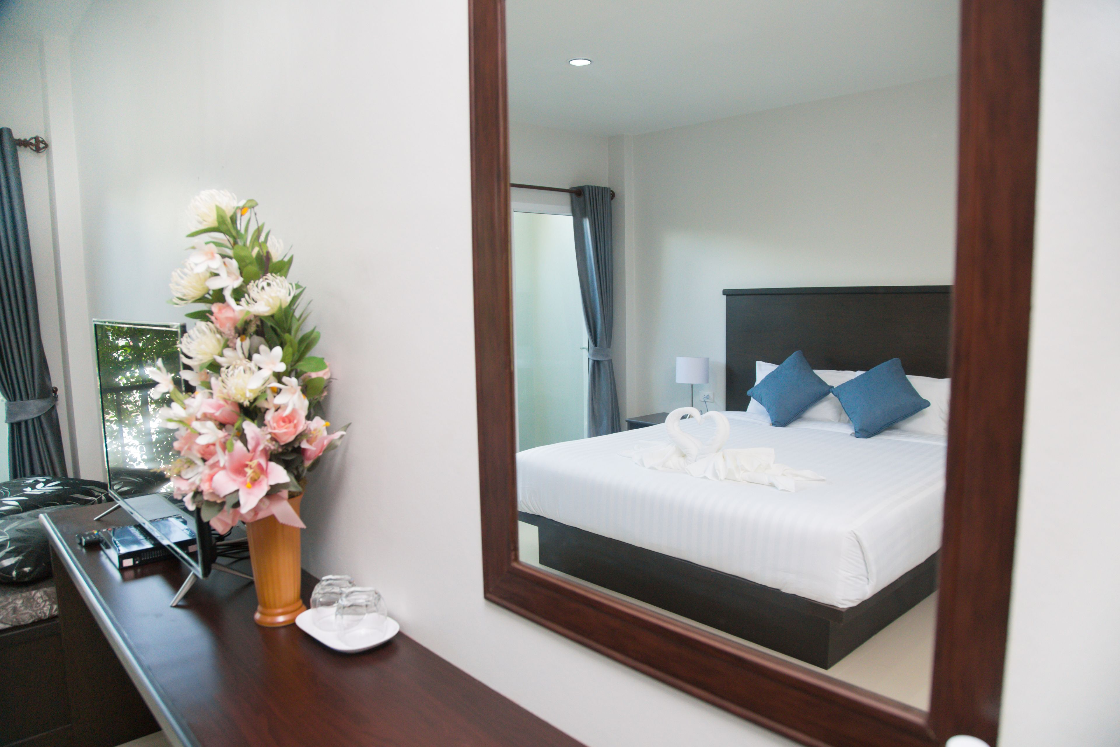A hotel room with a bed, a mirror, a desk with a vase of flowers, and a window with curtains.