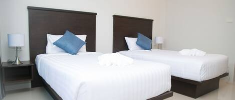 Two single beds with dark headboards, white bedding, and blue pillows. Each bed has a bedside table with a lamp.