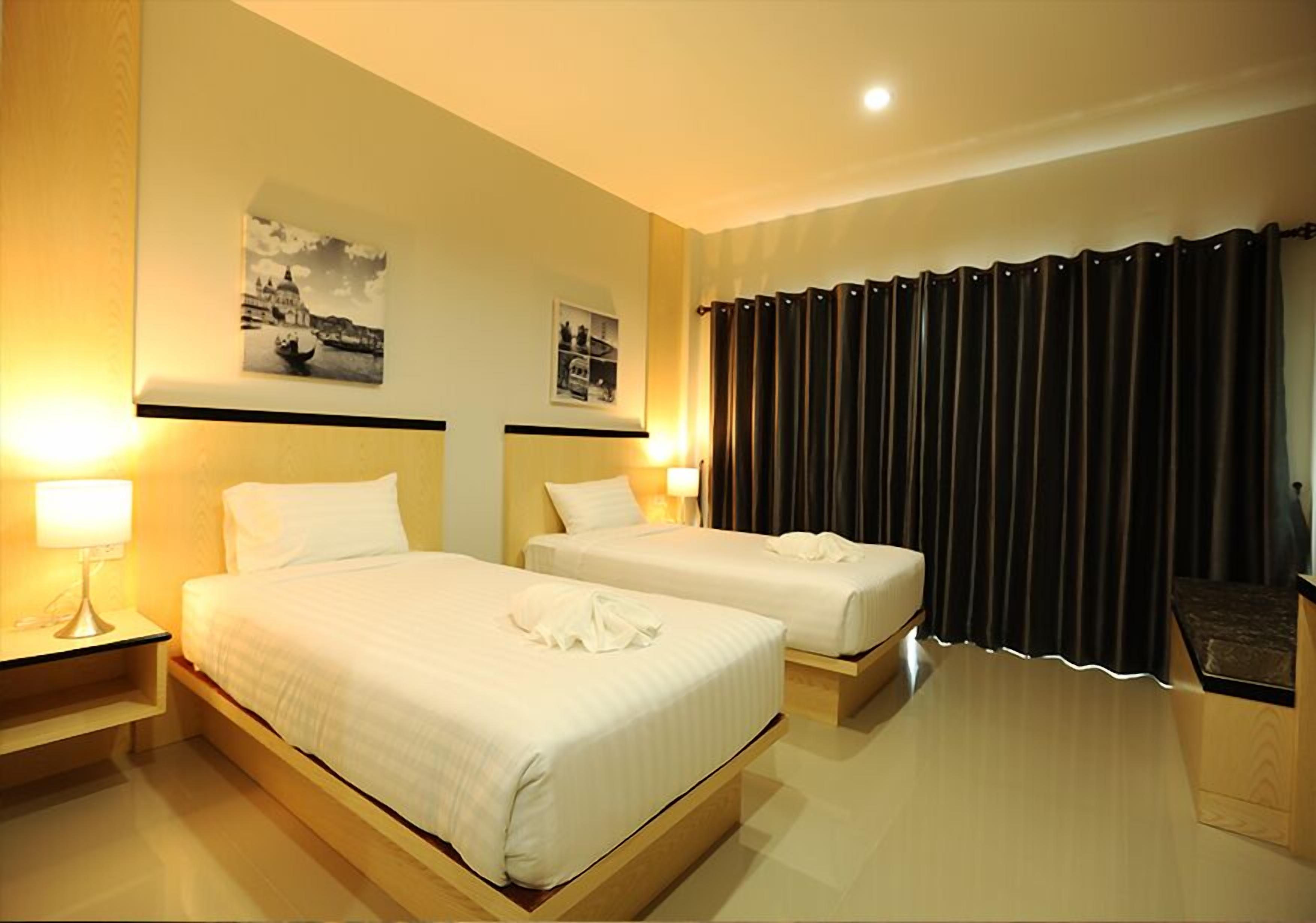 Een hotelkamer met twee bedden, een nachtkastje met een lamp en twee ingelijste foto's aan de muur.
