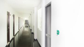 A long, narrow hallway with a fire exit sign, a red emergency alarm, and a door at the end.