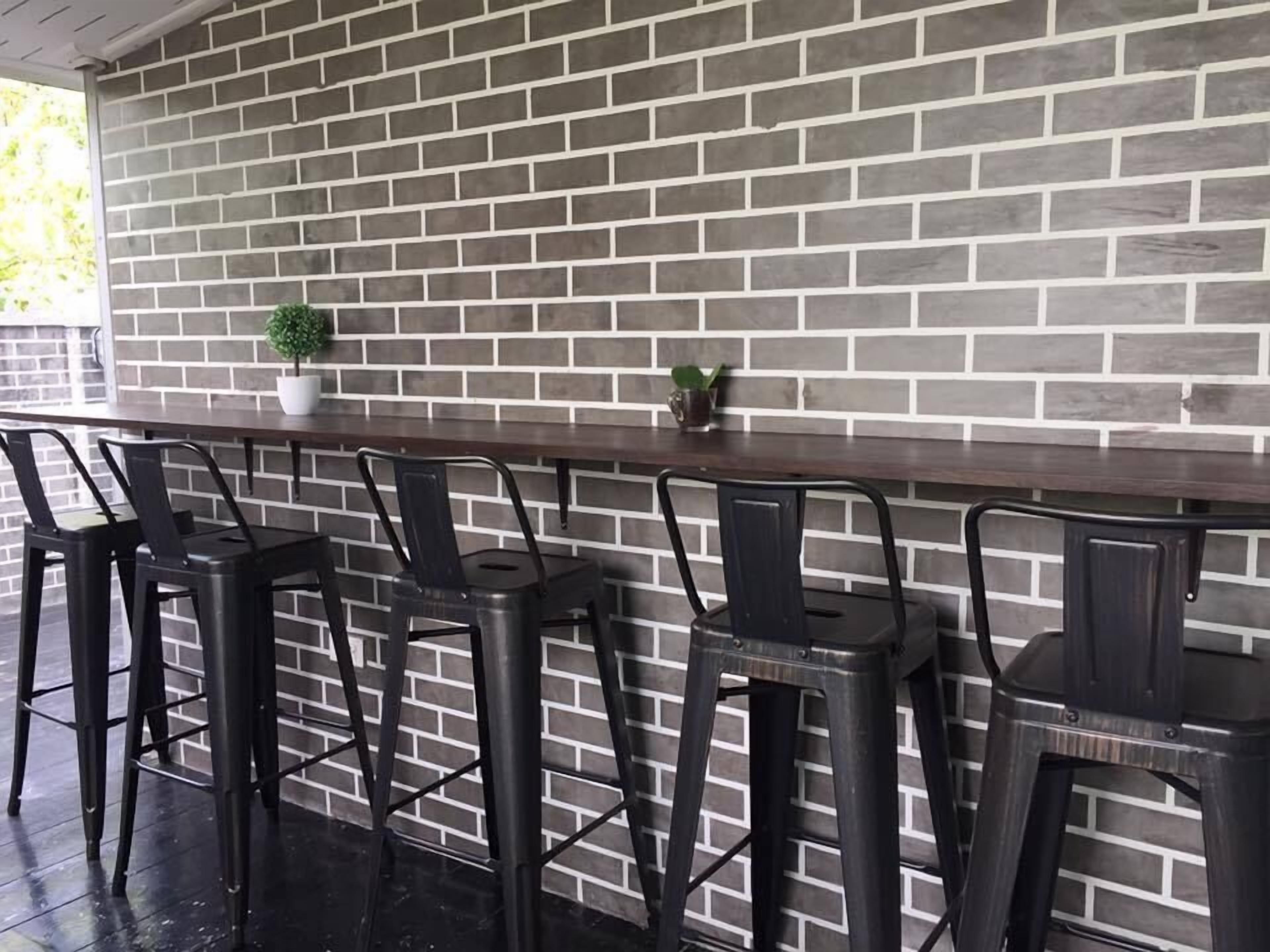A bar area with a brick wall backdrop, metal bar stools, and a small potted plant.