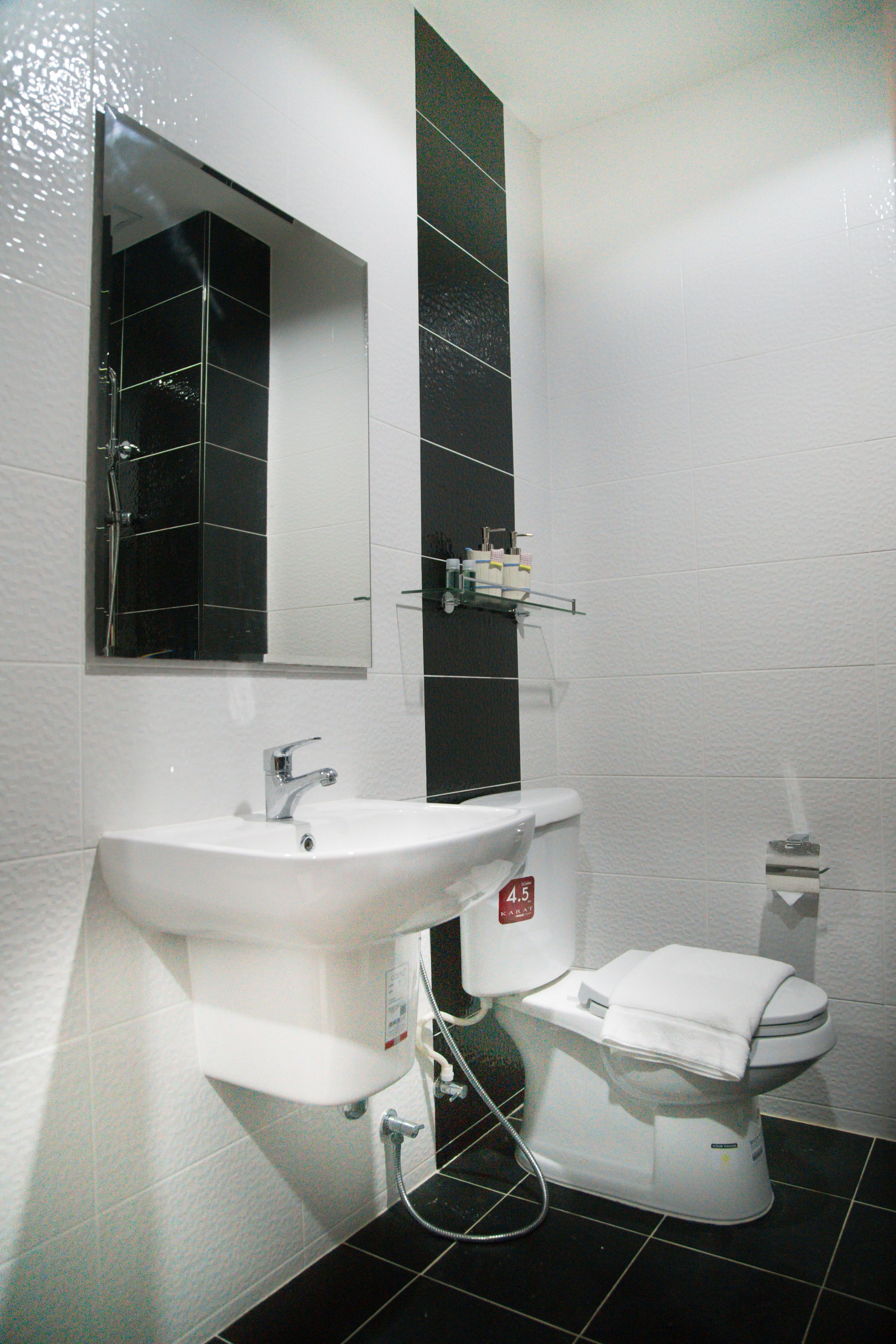 A bathroom with a white sink, a mirror, a toilet, and black tiled walls.