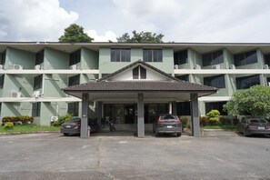 A multi-story building with a covered entrance, air conditioning units, and parked cars. - Sport Inn (Chiang Rai)