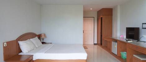 A hotel room with a wooden bed, a nightstand, a desk with a computer, a TV, and a door leading to another room.