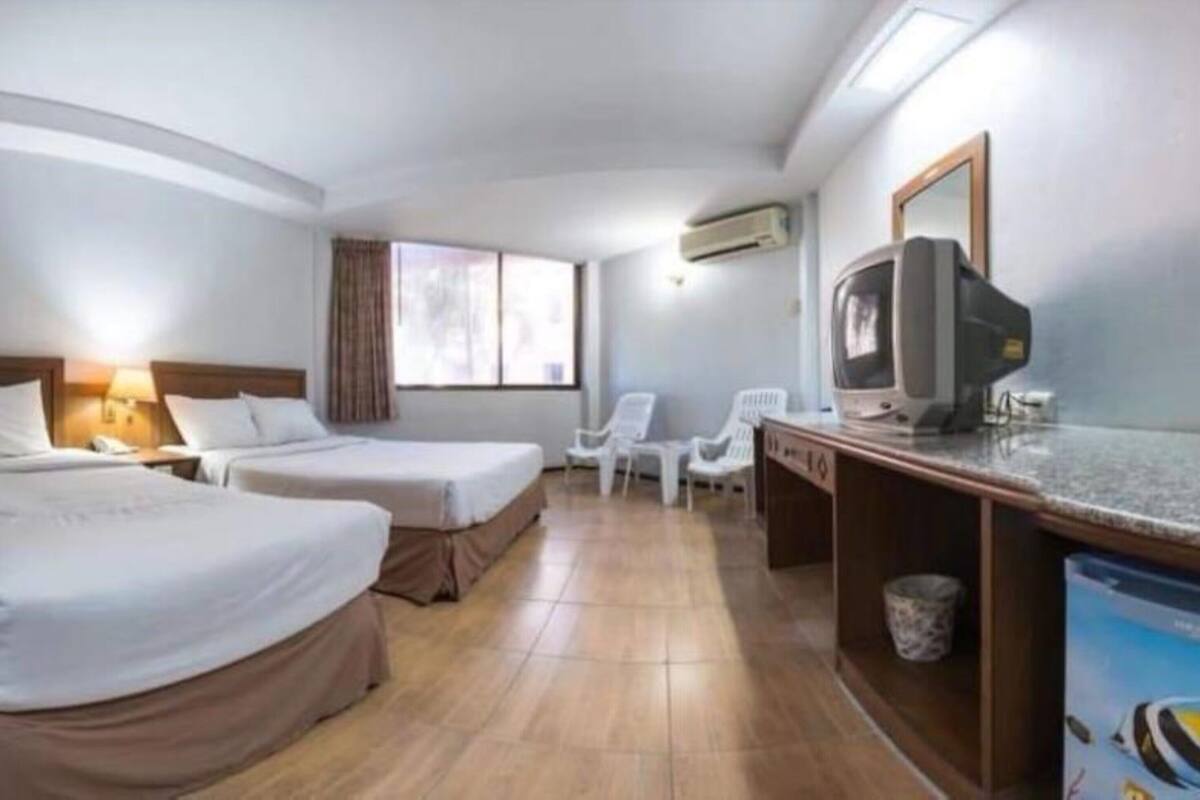 Ein Hotelzimmer mit zwei Betten, einem Schreibtisch, einem Fernseher, einem Stuhl und einem Fenster.