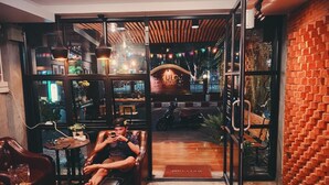 A cozy interior with a leather couch, a wooden coffee table, and a glass door leading to an outdoor area with a motorcycle. - 84 Gallery - Hostel (Chiang Mai)