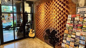 A room with a guitar, a fan, and a brick wall with a brick pattern. - 84 Gallery - Hostel (Chiang Mai)