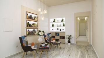 A modern living room with a marble floor, a coffee table, two chairs, a bookshelf, and a potted plant.