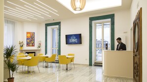 A hotel lobby with a reception desk, a fireplace, and a dining area with yellow chairs and tables. - The Five Rooms Napoli (Naples)