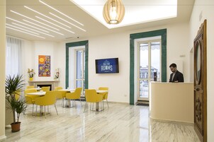 Een hotel lobby met een receptiebalie, een open haard en een eetgedeelte met gele stoelen en tafels.