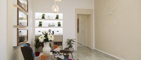 A dining area with a table, chairs, and hanging lights. There are shelves with decorative items and a clock on the wall.