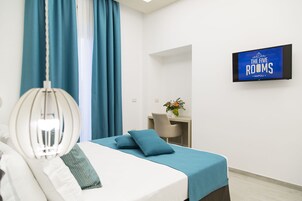 Een hotelkamer met een bed, een bureau en een televisie waarop 'The Five Rooms Napoli' staat.