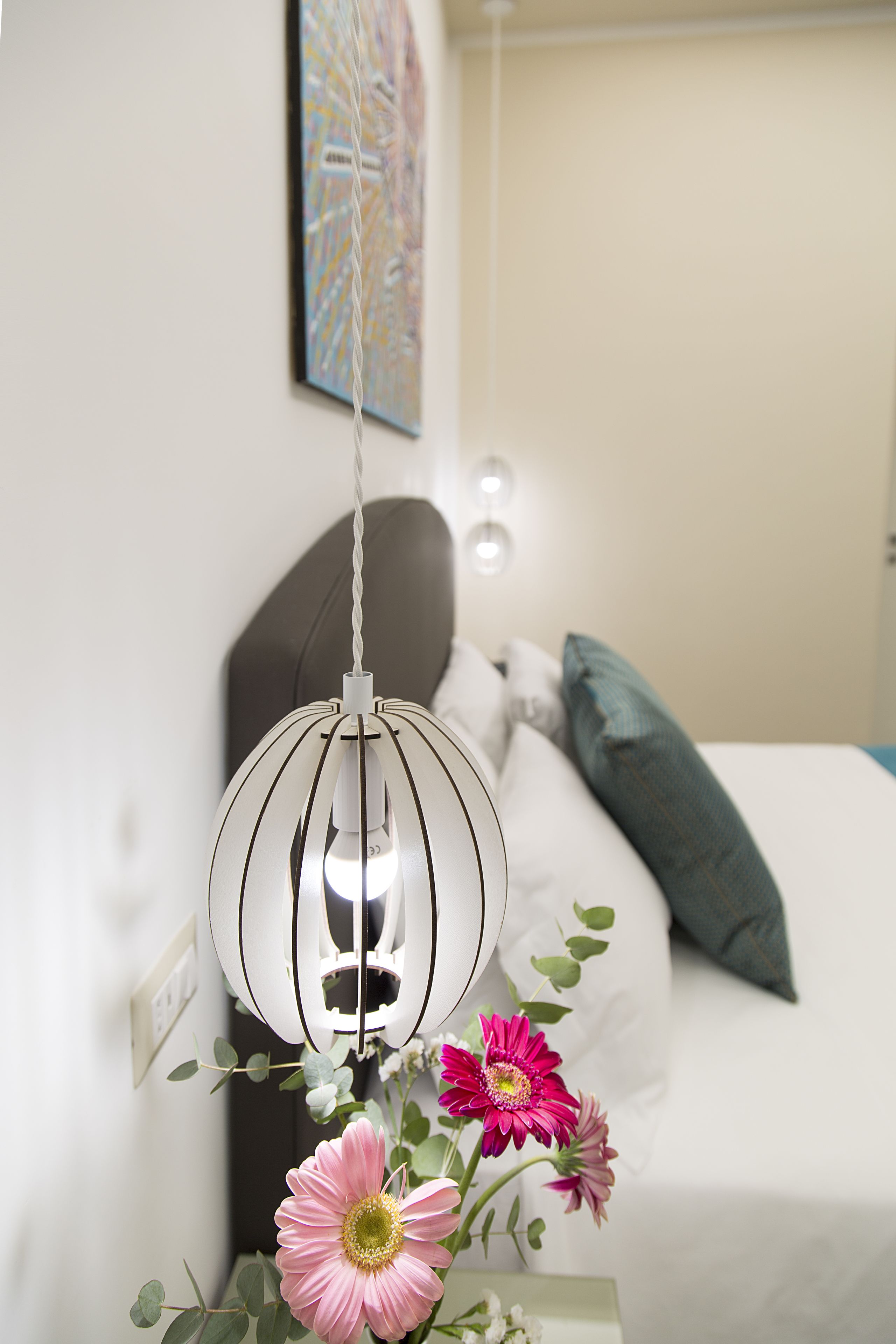 A modern bedroom with a bed, a hanging light fixture, and a wall-mounted artwork.