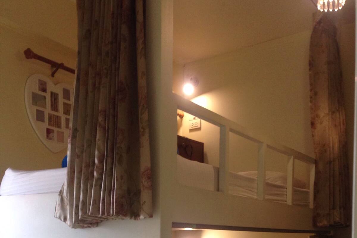 Habitación con literas, una escalerilla de madera, mesita de noche con lámpara y un adorno en la pared.