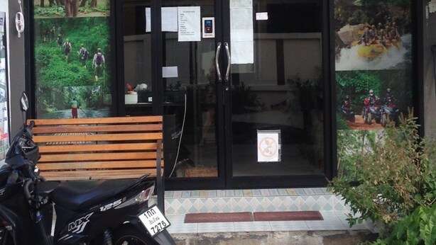 A building with a black facade, glass doors, and a wooden bench outside. - Smile Capsule Hostel (Chiang Mai)