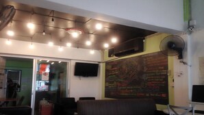 A room with a couch, a table, a TV mounted on the wall, and a chalkboard with writing. - Smile Capsule Hostel (Chiang Mai)
