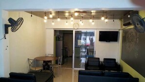 A modern lounge area with a round table, multiple seating options, and a large screen. - Smile Capsule Hostel (Chiang Mai)