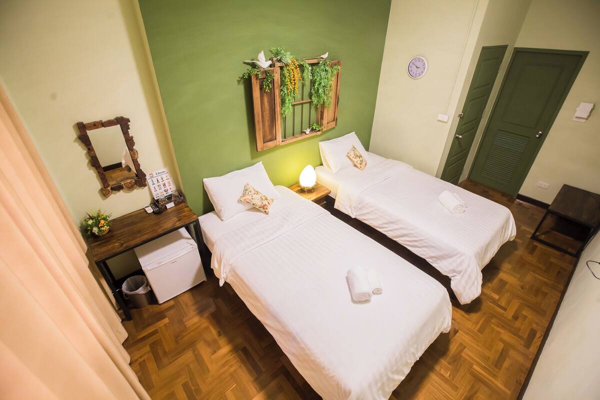 A room with two beds, a wooden desk, a mirror, and a wall-mounted plant.