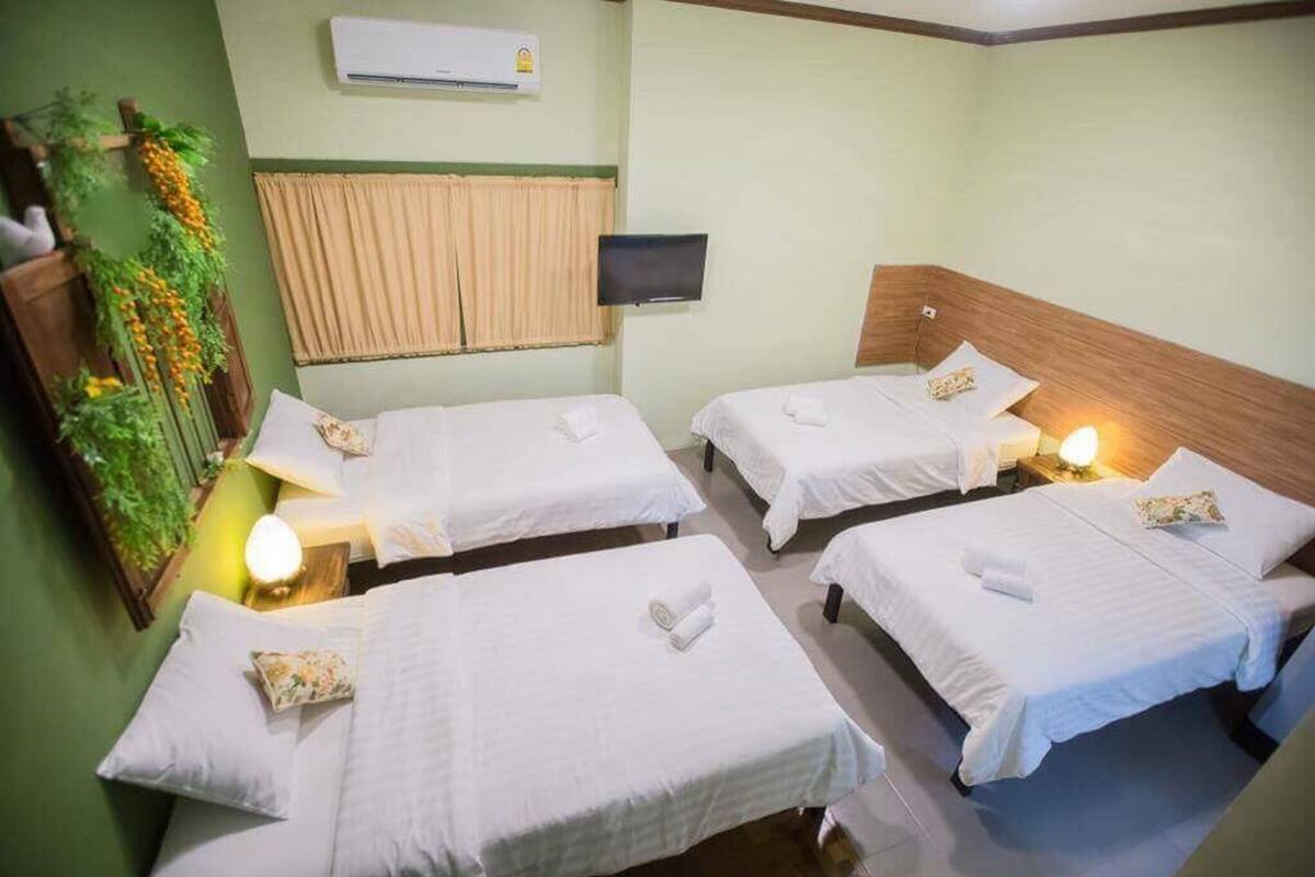 A hotel room with four single beds, a television, an air conditioning unit, and a decorative plant.